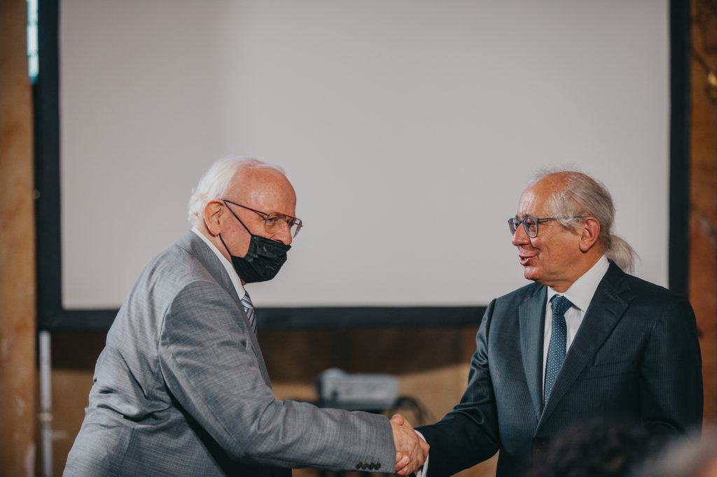 Dwóch siwych mężczyzn w okularach ubranych w marynarki, uściskujących sobie dłonie