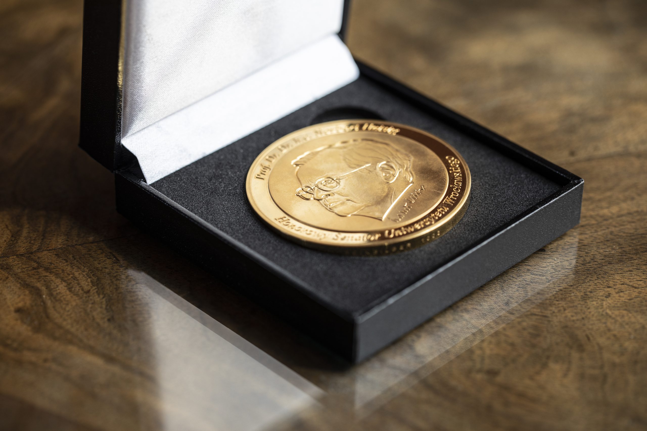 srebrny okrągły medal z wizerunkiem głowy mężczyzny w okularach