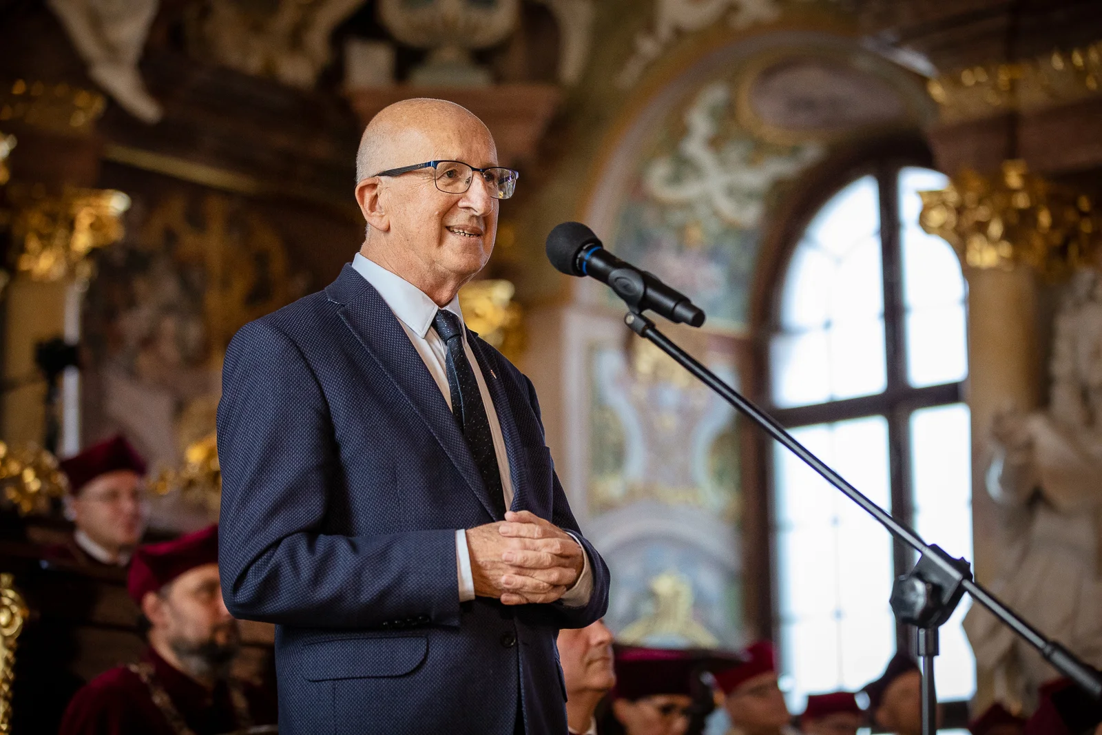 starszy mężczyzna w garniturze stoi przed mikrofonem